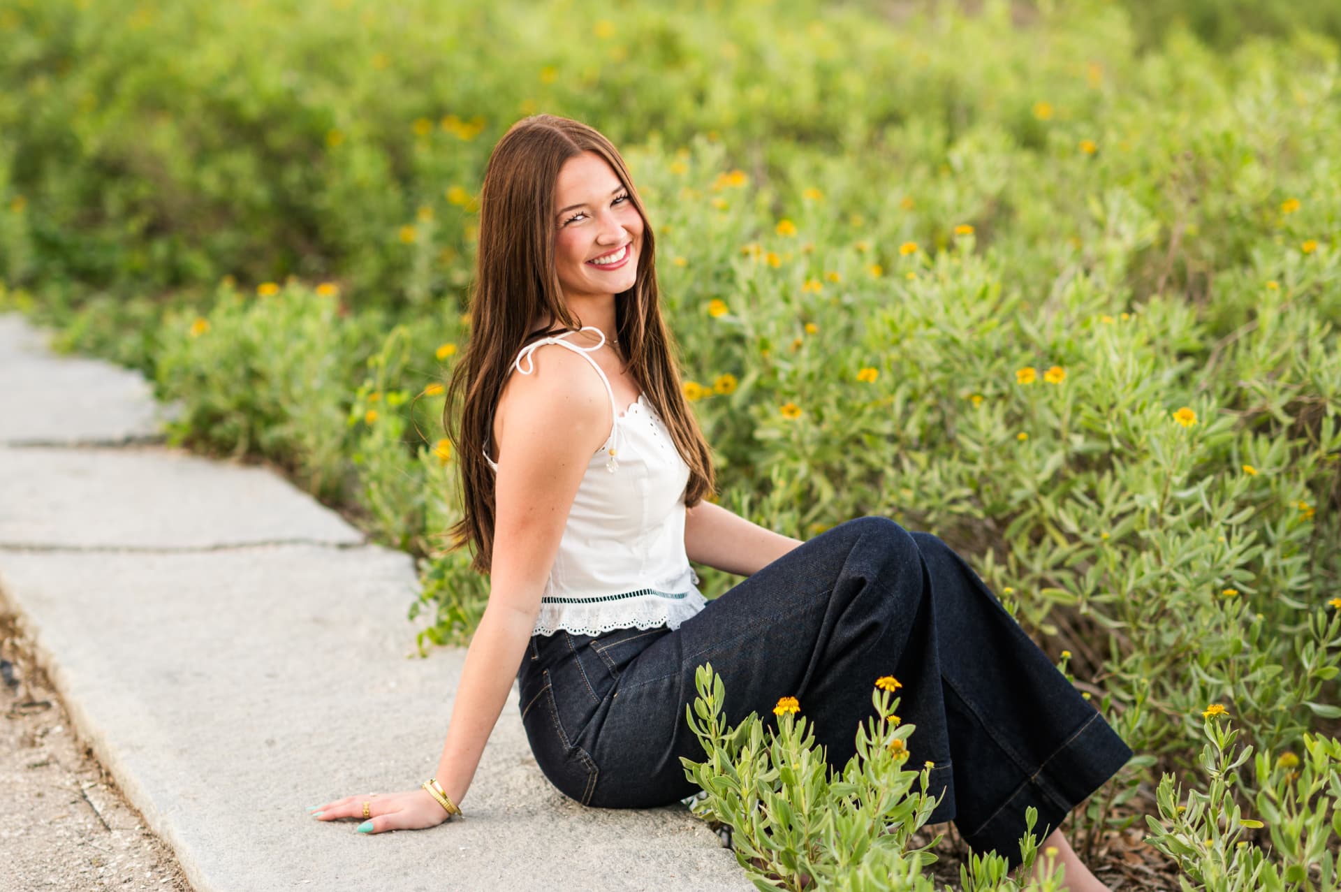 Senior portrait of Em sitting among yellow wildflowers and greenery